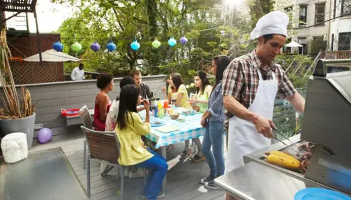 A man in an apron grills while 5 people site around a table talking in their outdoor amenities