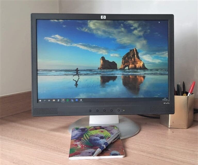 Image of computer screen with notebook and pen in the front and a gold pot of pens to the right