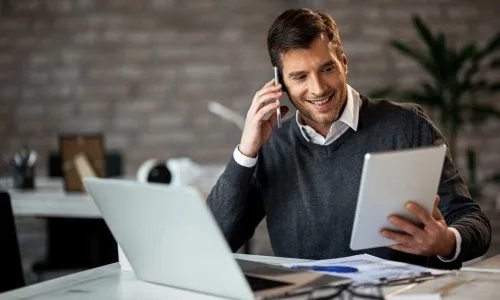 White male using HOA board member software on an iPad while holding a phone and seated in front of a computer.