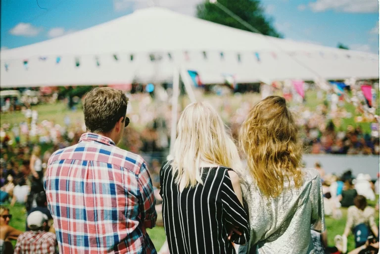 Putting into practice an HOA social committee idea: Three individuals, one man and two women, stand together looking towards an cheerful event at ther HOA with a tent and colorful decorations.